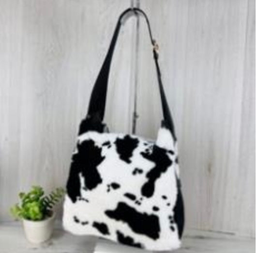 Black and white cow print handbag on a light wooden surface with a blurred background