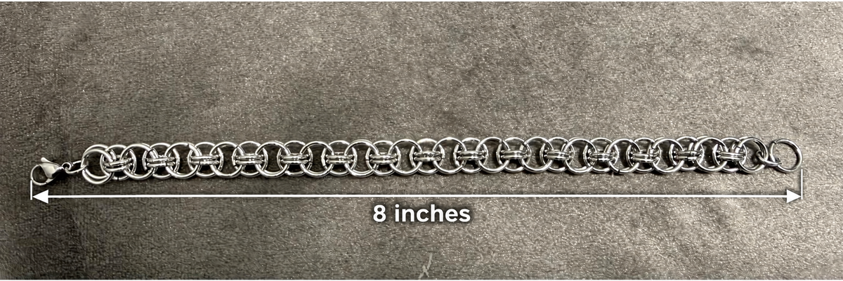 A silver metal link chain bracelet or collar shown flat on a textured gray background, with a white measurement arrow and text indicating 8 inches in length.