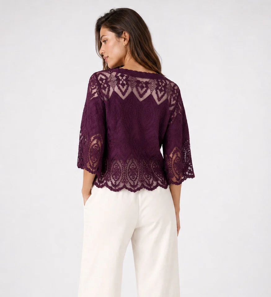 A woman shown from the back wearing a wine lace top with three-quarter sleeves and white pants, photographed against a plain light gray studio background.