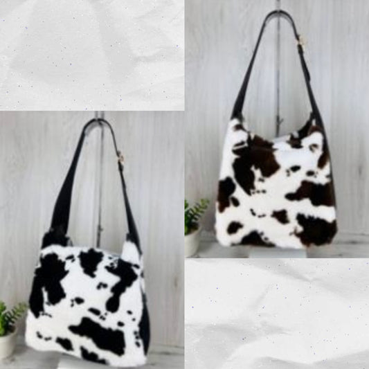 Black and white and brown and white  cow print handbag on a light wooden surface with a white background