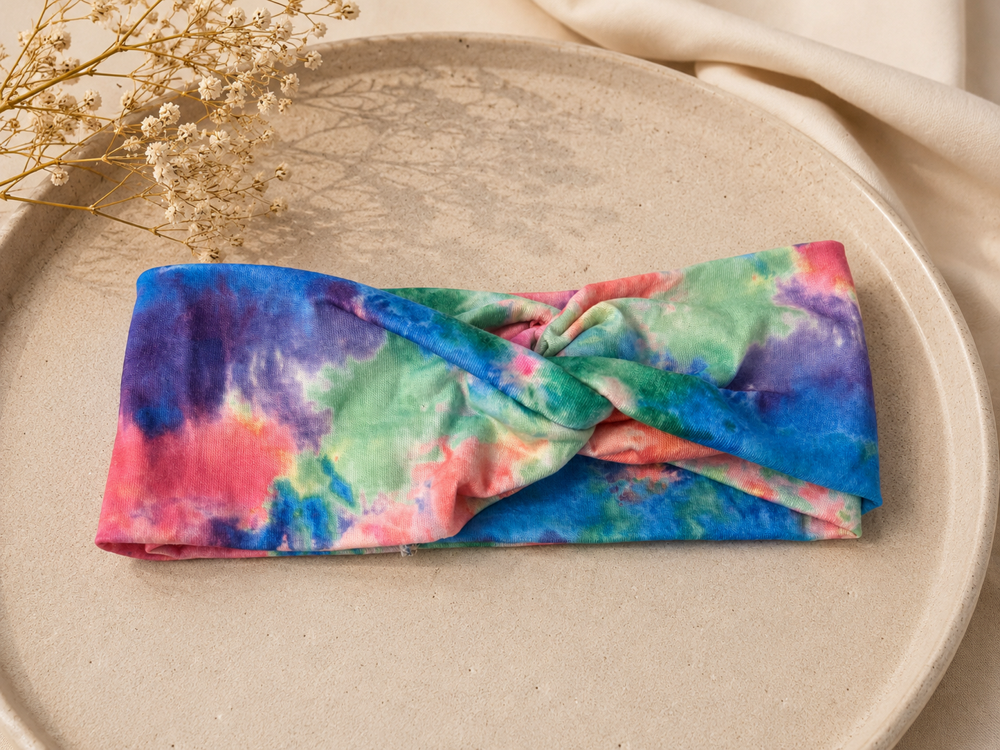 Colorful tie-dye headband on a beige plate with dried flowers.