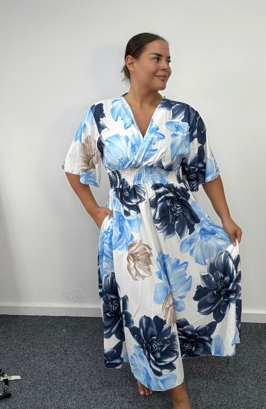 Woman wearing a blue and white floral dress against a plain background