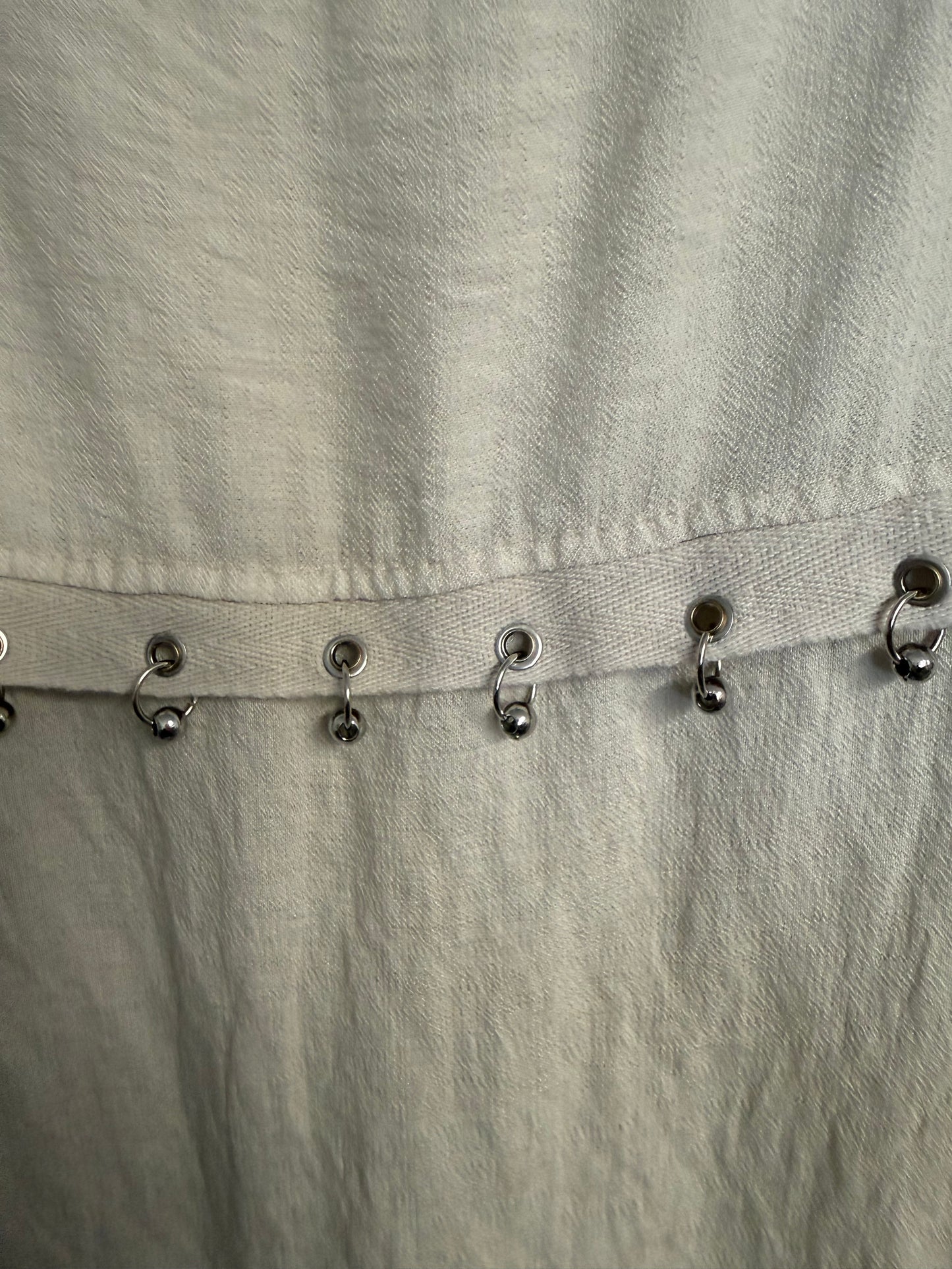 Close-up of a light beige textured fabric garment with a vertical row of metal rings with beads on.