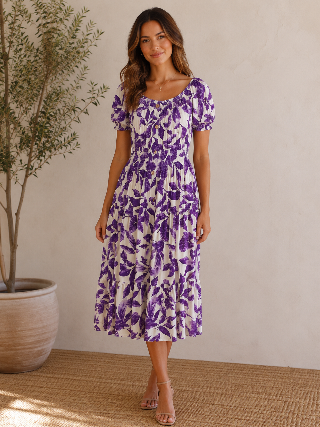 Woman wearing a purple floral dress standing indoors with a plant in the background