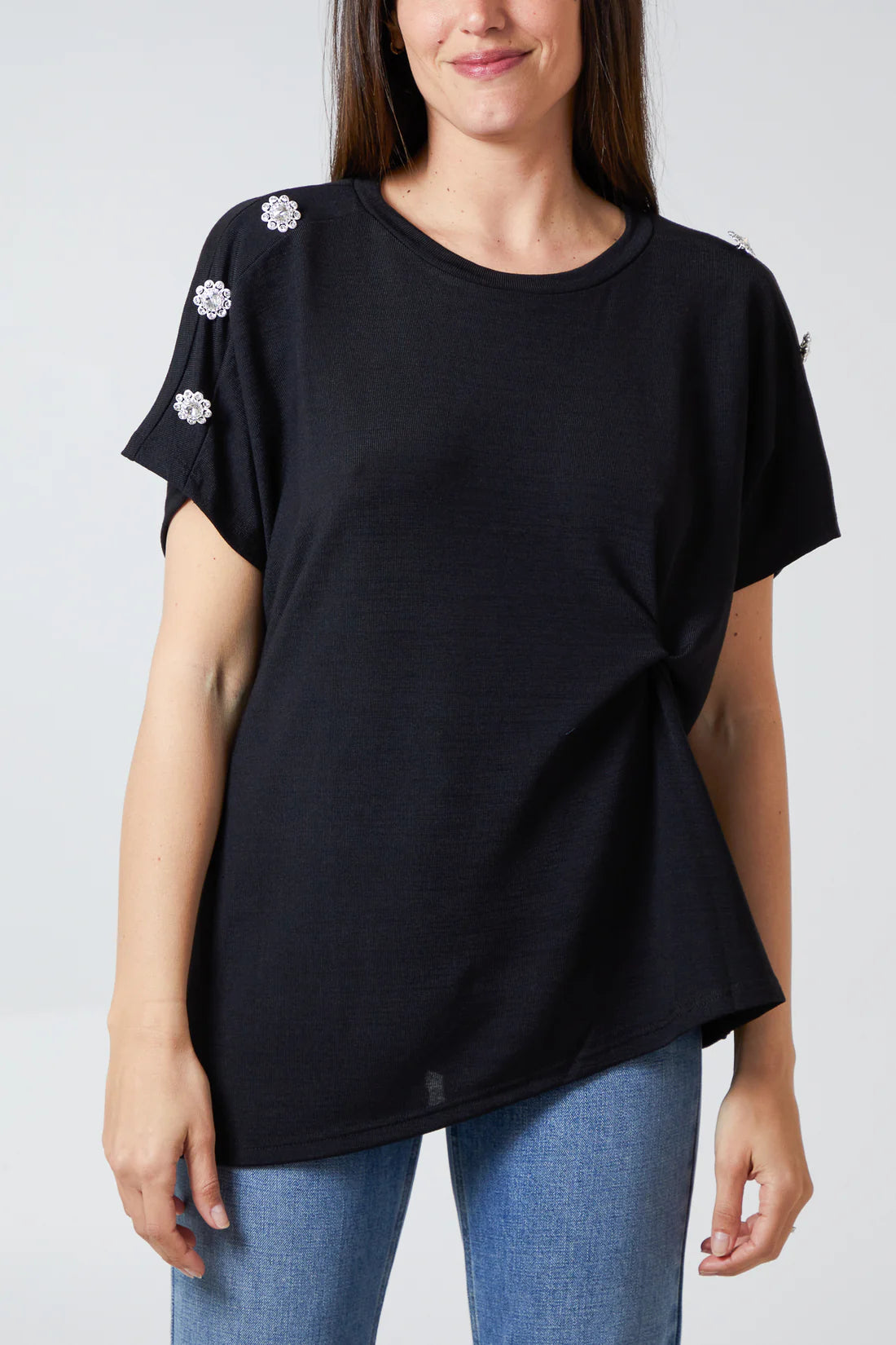 Woman wearing a black t-shirt with diamante flower button embellishments on a plain background