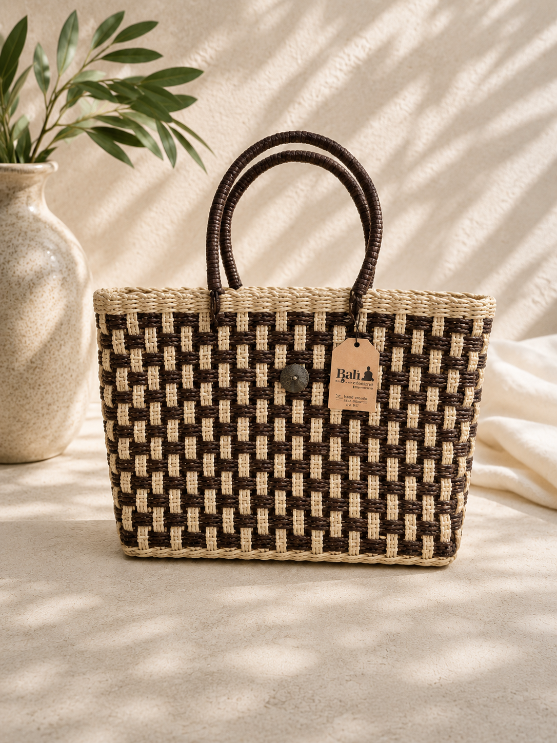 Woven handbag with a brand tag on a light surface with a plant in the background