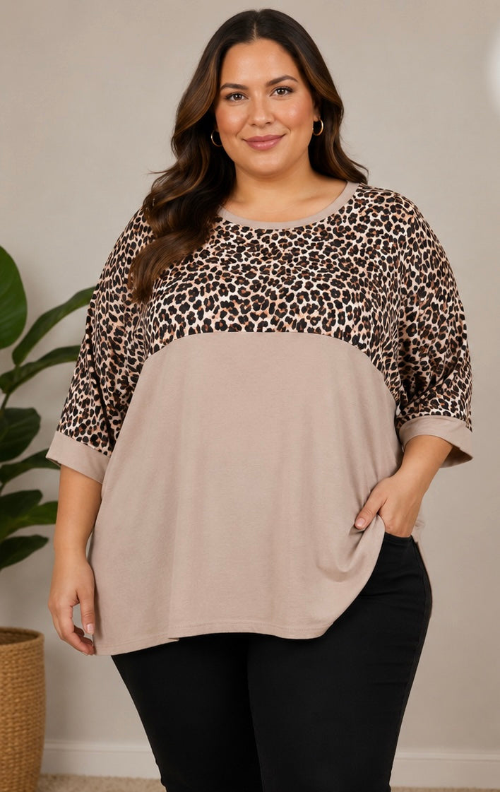 A woman modeling a colorblock top with a beige solid lower half and a brown, black, and beige leopard print upper half, paired with black pants.
