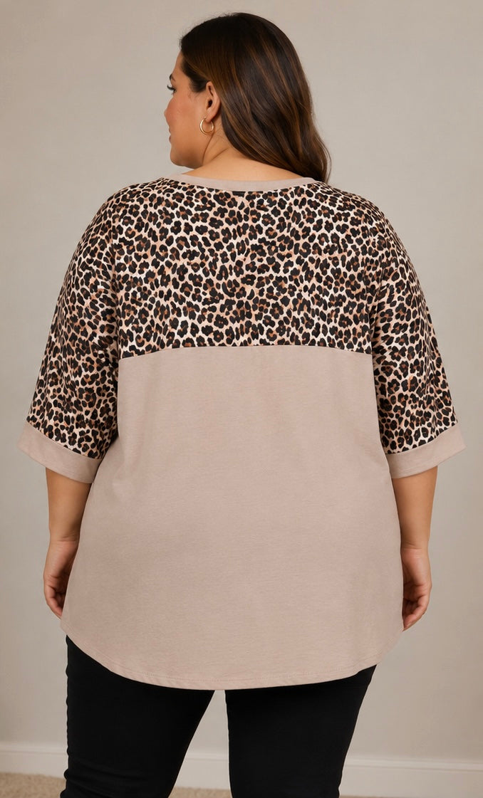 A woman shown from the back wearing a colorblock top with a beige body and leopard print sleeves and upper back, paired with black pants, against a plain beige wall.