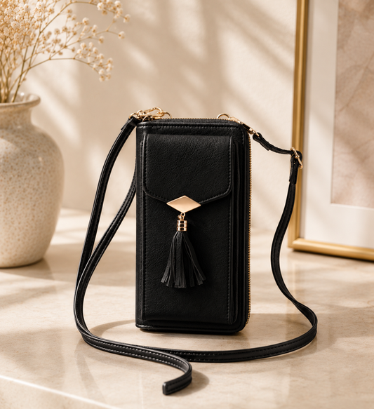 Black crossbody bag with a tassel on a light wooden surface.