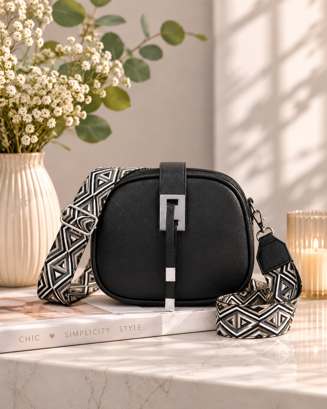 Black bag with patterned strap on a marble surface with books and a vase in the background