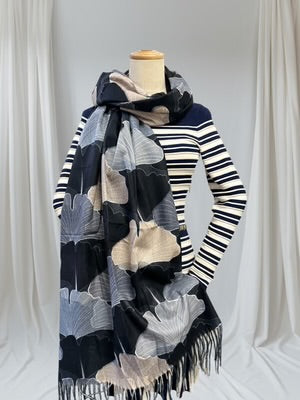 Mannequin wearing a striped sweater and a large, patterned scarf against a white curtain background