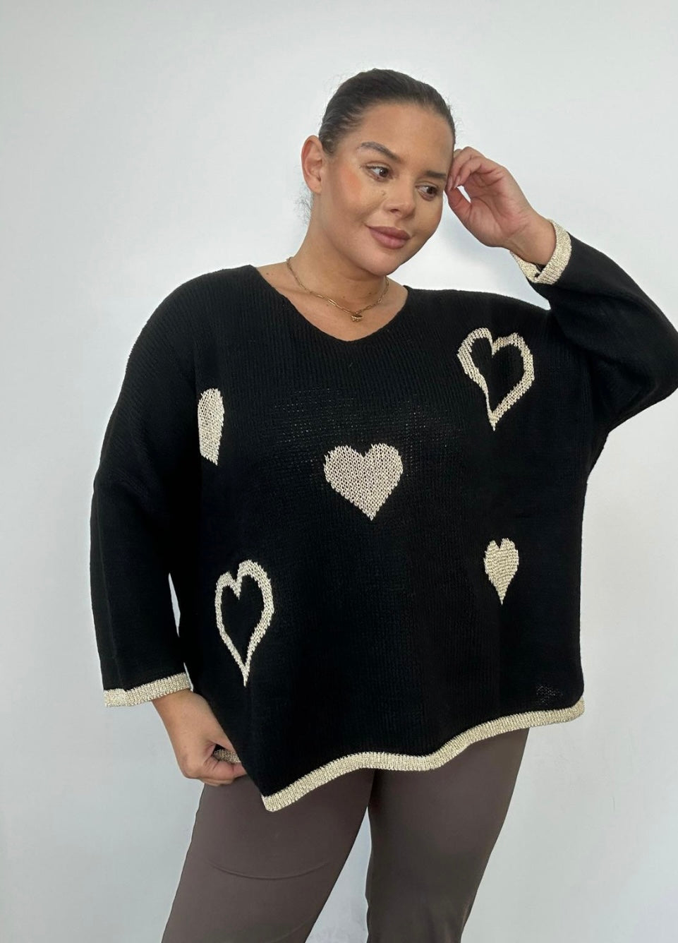 Woman wearing a black sweater with heart patterns on a plain background