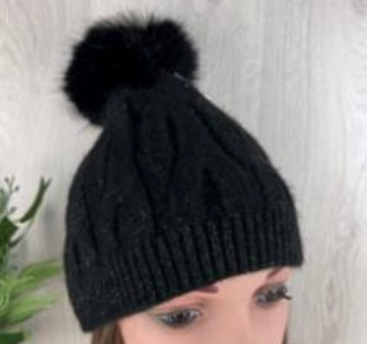 Black knit beanie with pom-pom on a neutral background