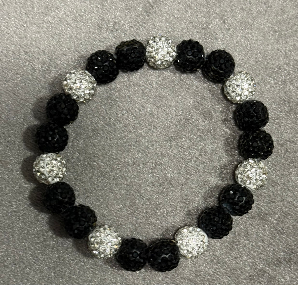 A beaded stretch bracelet featuring alternating black faceted beads and silver faceted crystal beads, displayed on a textured gray background.