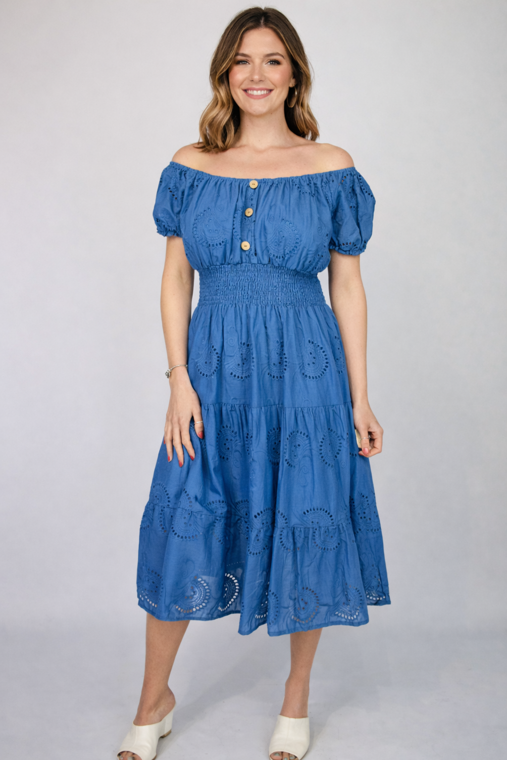 Woman wearing a Blue Broderie Anglaise Bardot Midi Dress with puff sleeves on a gray background