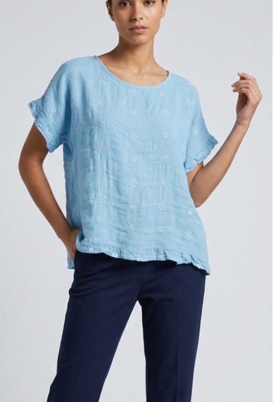 Woman wearing a light blue top and navy pants on a plain background