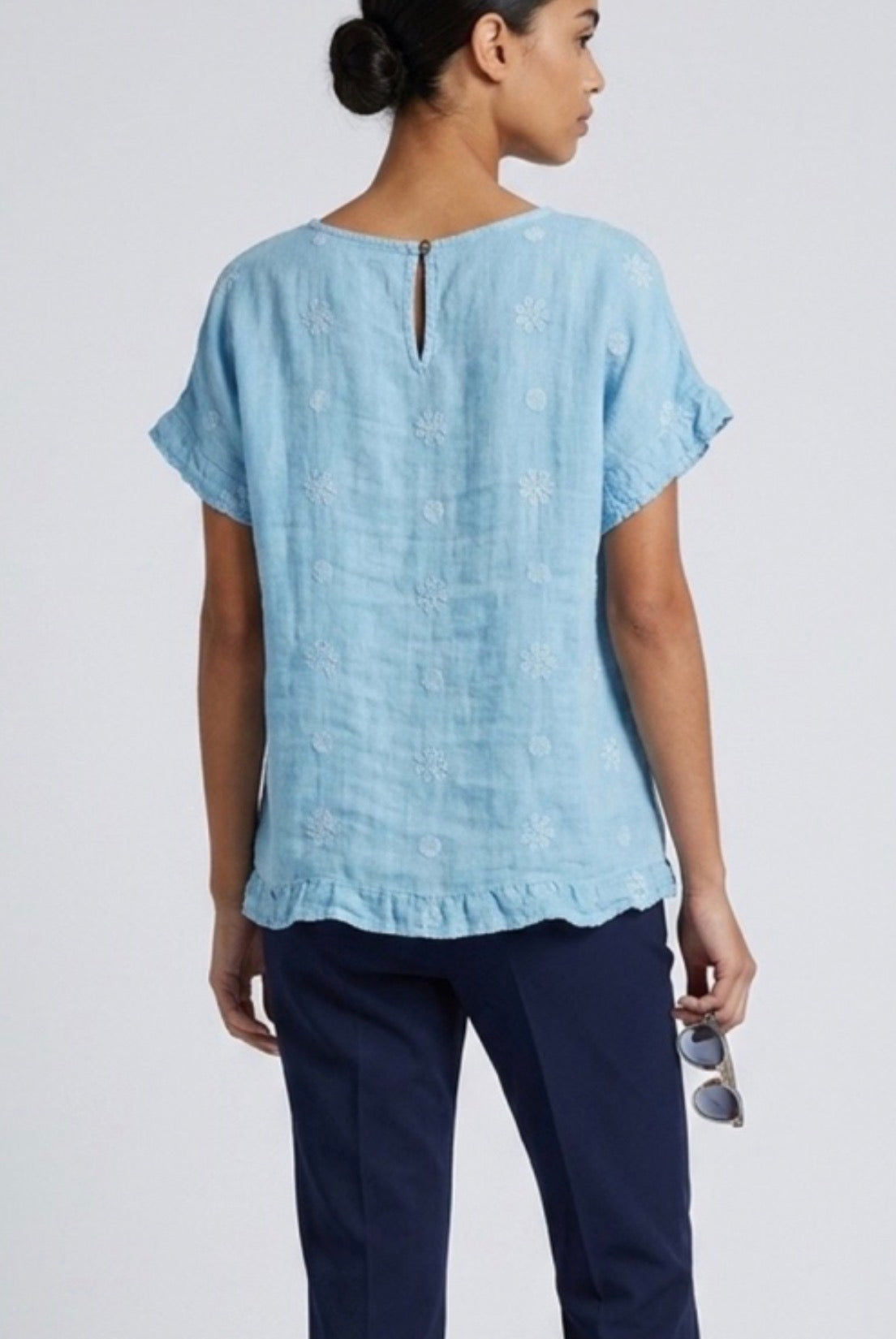 Back view of Woman wearing a light blue top and dark pants against a white background