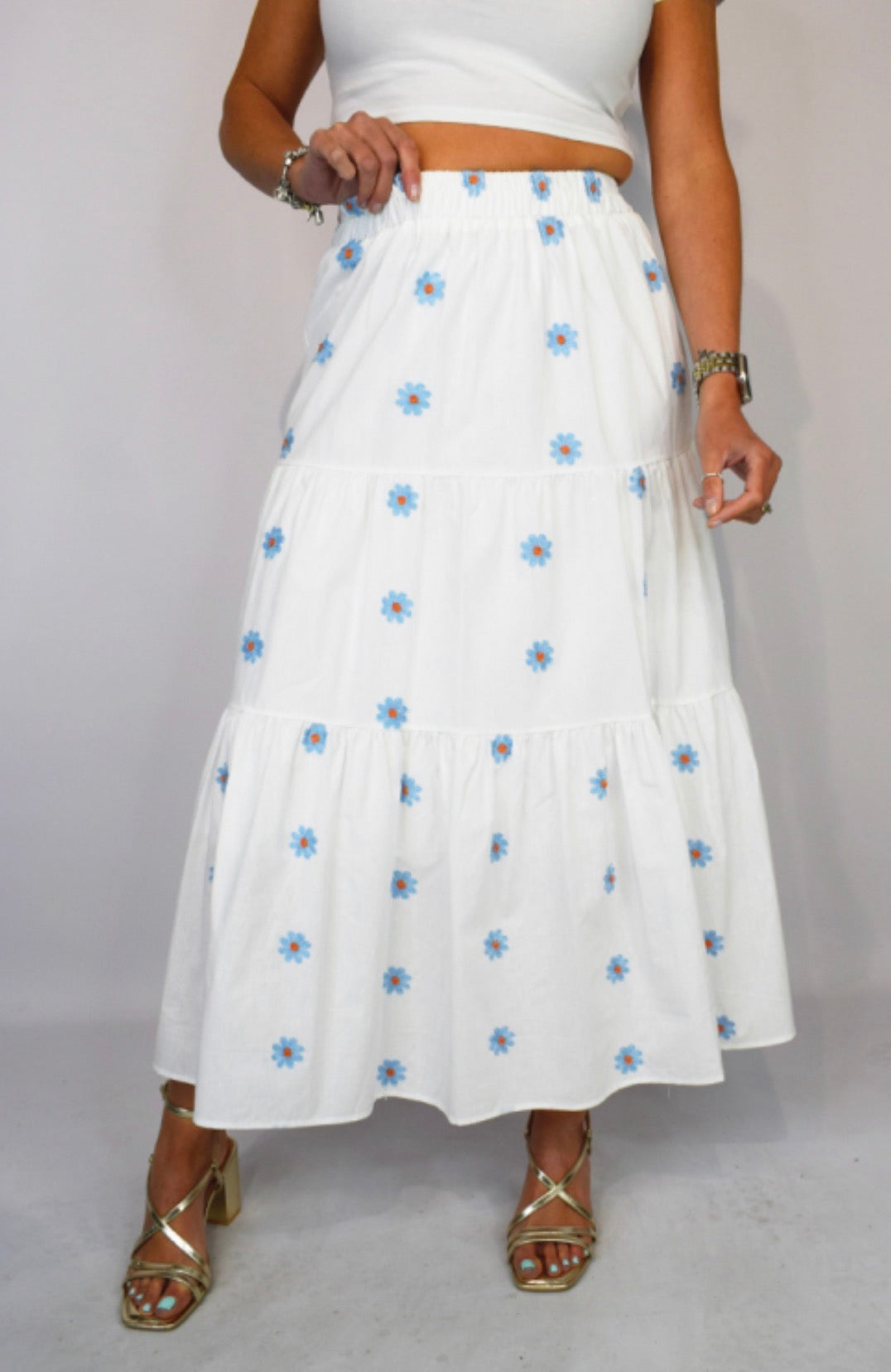 White skirt with blue floral pattern worn by a person on a plain background