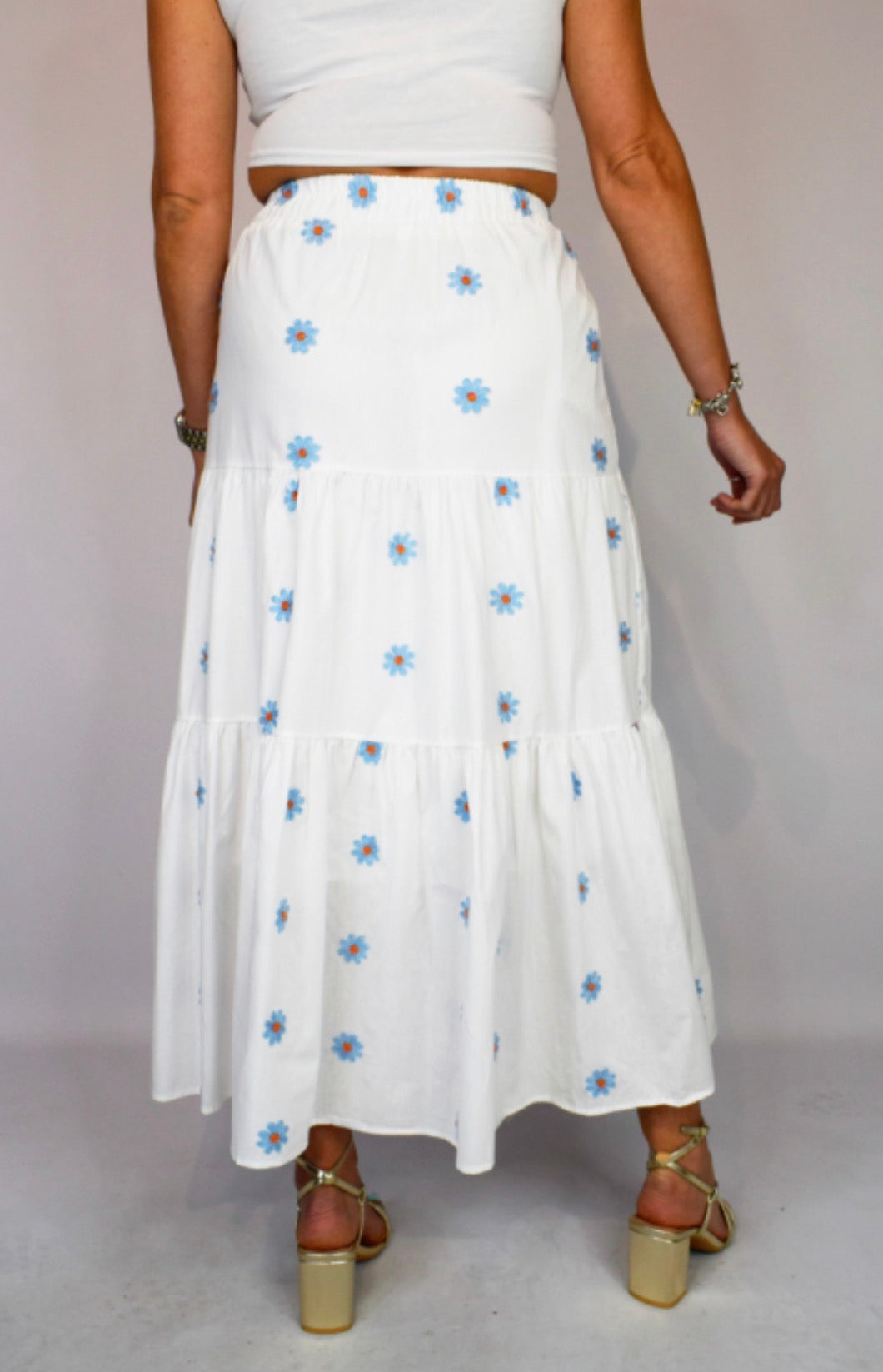 White skirt with blue floral patterns worn by a person on a plain background