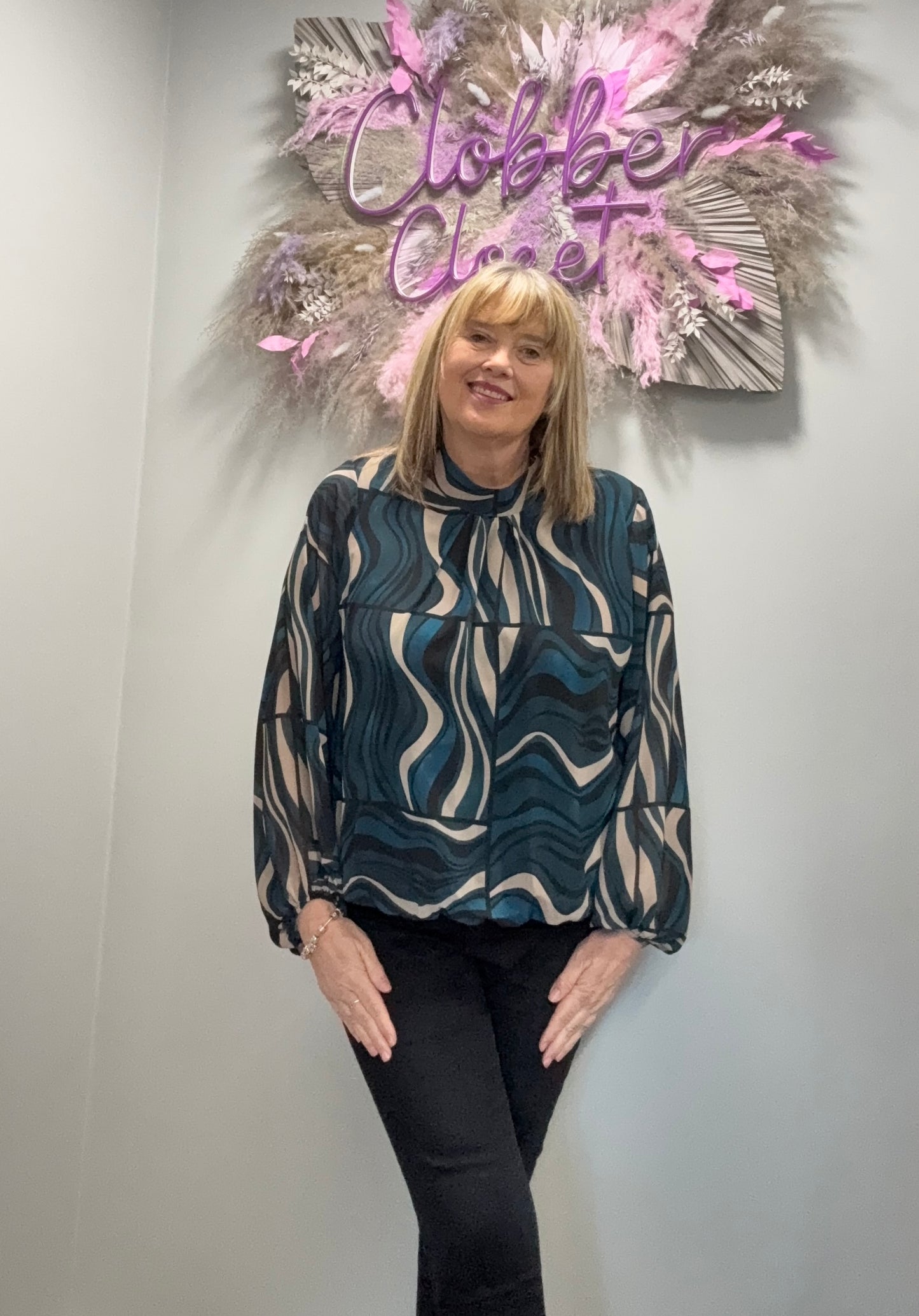 Woman standing in front of a decorative wall with 'Clobber Clozet' sign