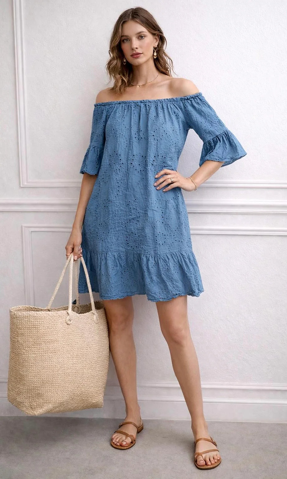 Woman wearing a blue Italian Broderie Anglaise Dress/Top holding a beige tote bag against a white wall.