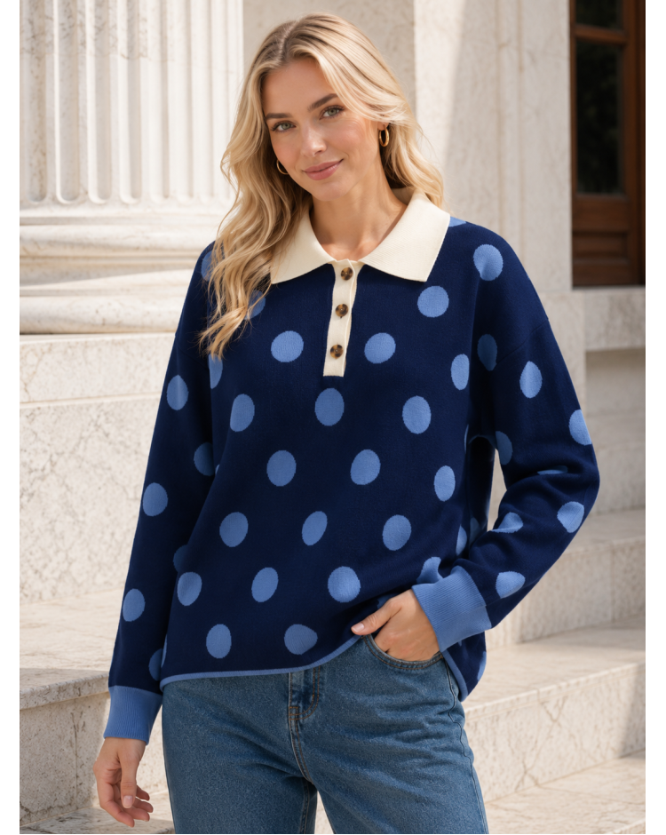 A woman wearing a navy blue long-sleeve knit sweater with large light blue polka dots and a cream collar, paired with blue jeans, standing on stone steps.