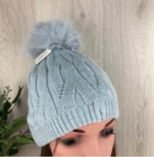 Light blue knitted beanie with a pom-pom on a neutral background