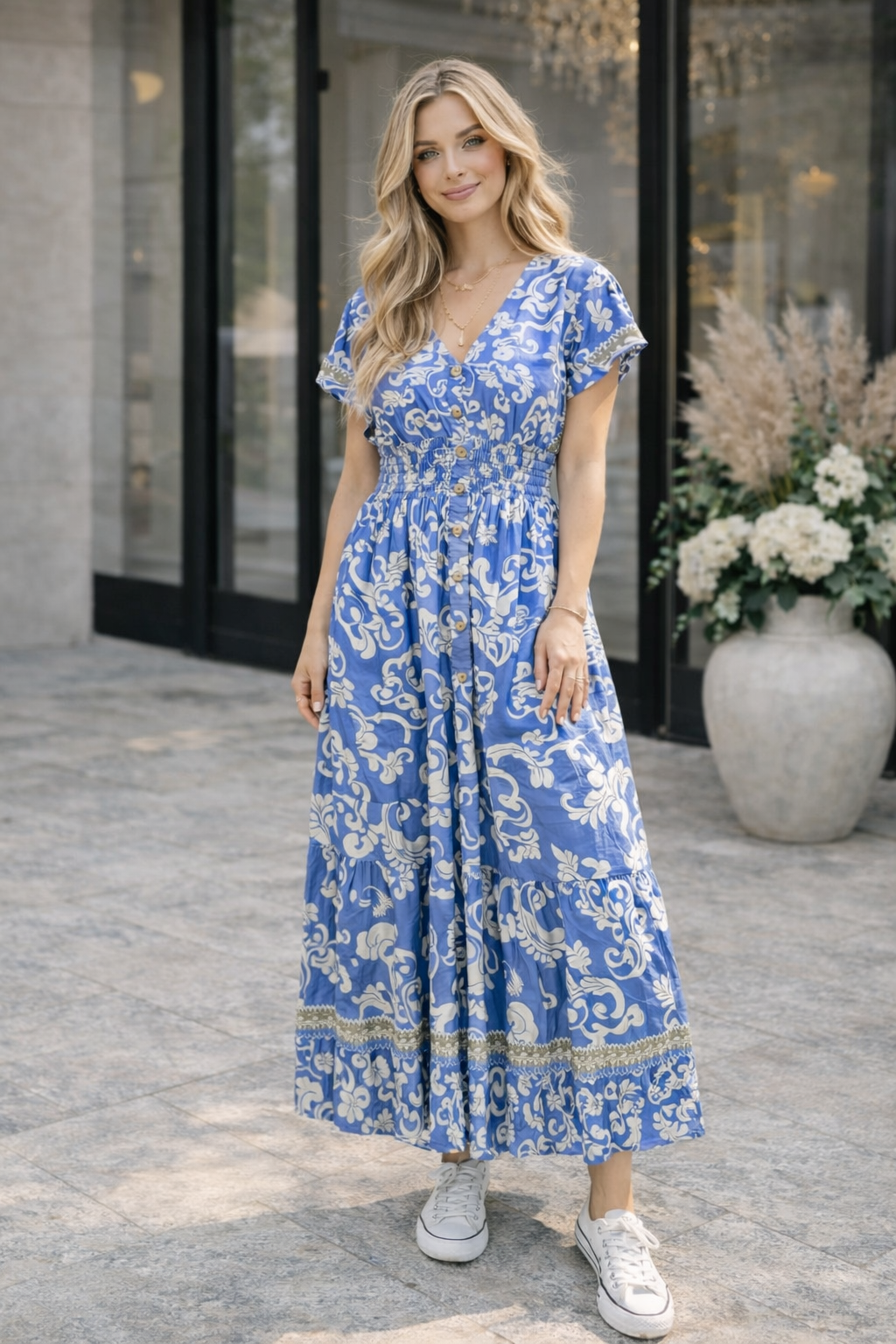 Woman wearing a blue Retro V Neck Floral Maxi Dress standing outdoors with a building and flowers in the background.