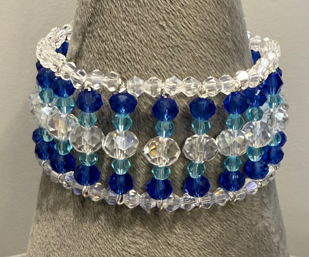 A multi-strand beaded bracelet displayed on a gray fabric jewelry stand. The bracelet features faceted beads in royal blue, sky blue, and clear crystal, separated by small silver spacer beads.