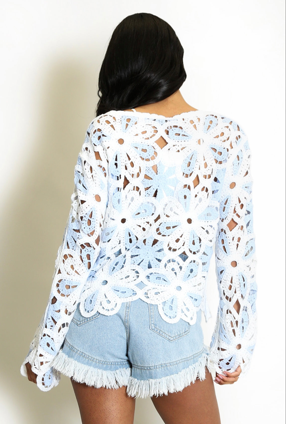 Back View of Woman wearing a Blue and White Floral Crochet Jumper and denim shorts against a plain background