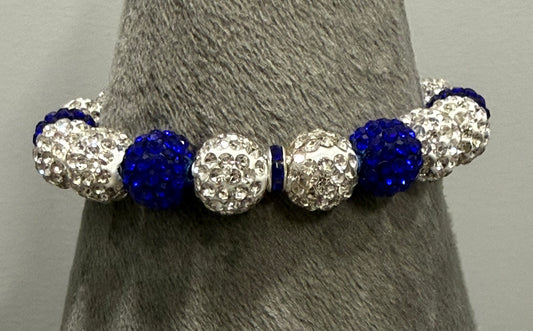 A beaded stretch bracelet displayed on a gray textured cone stand. The bracelet features alternating deep royal blue faceted beads and silver rhinestone-covered round beads.
