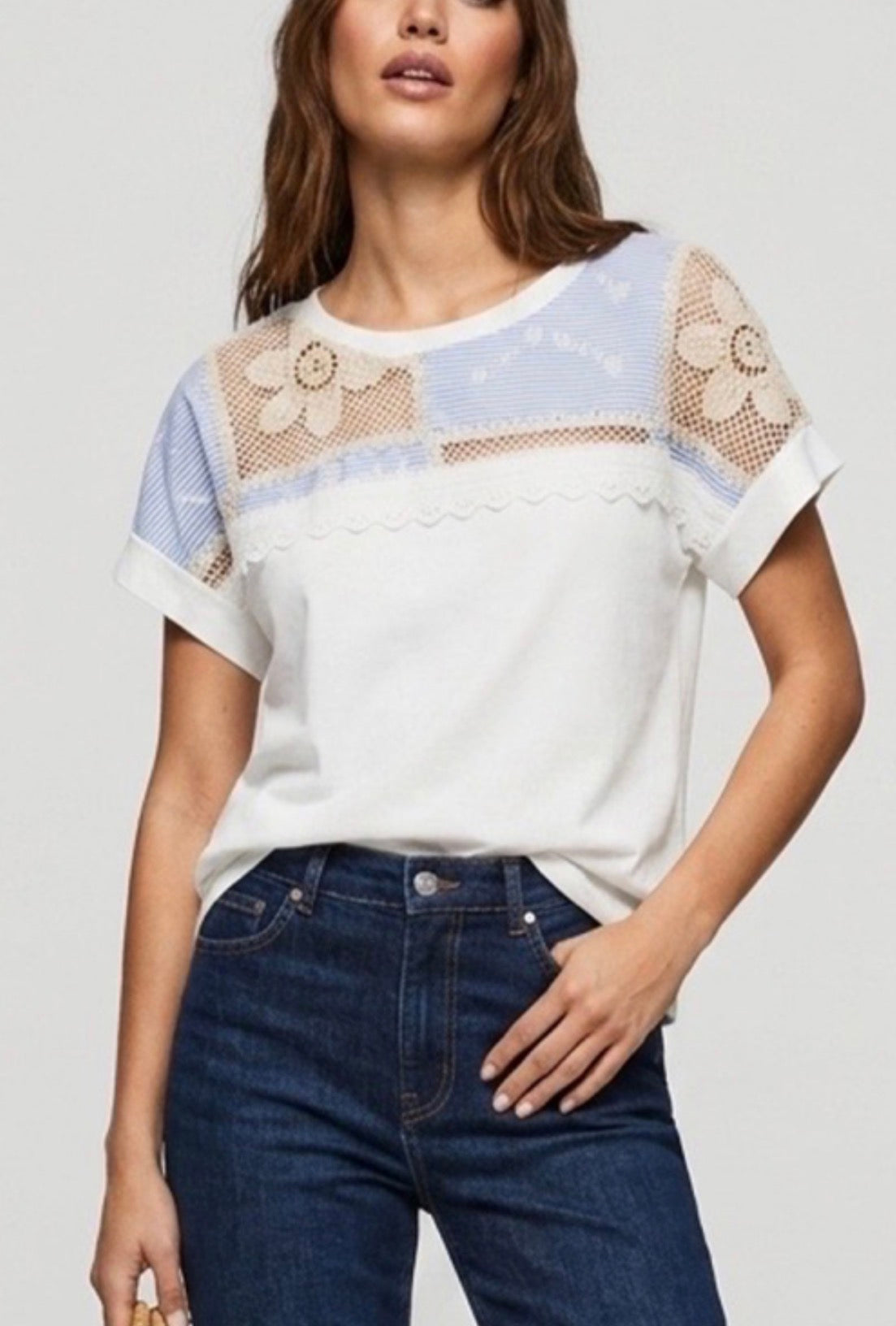 Woman wearing a white t-shirt with floral mesh sleeves and blue jeans on a light gray background