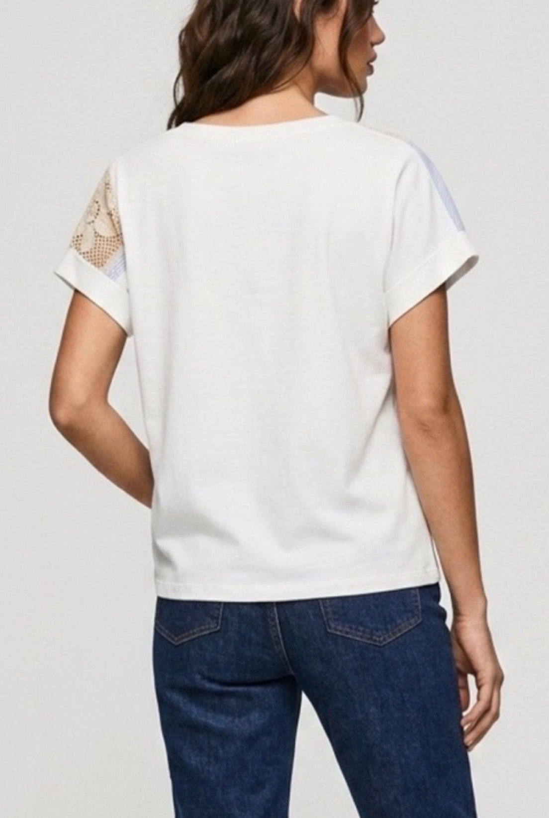 Back view of Woman wearing a white top with lace sleeves and blue jeans on a plain background
