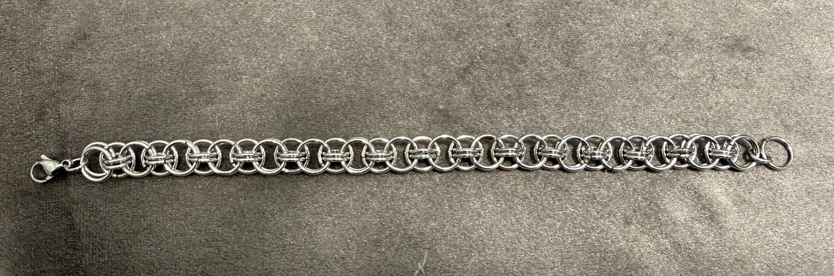 A silver-tone metal chain link bracelet with a lobster clasp and a small ring accent on the opposite end, displayed horizontally on a textured gray surface.
