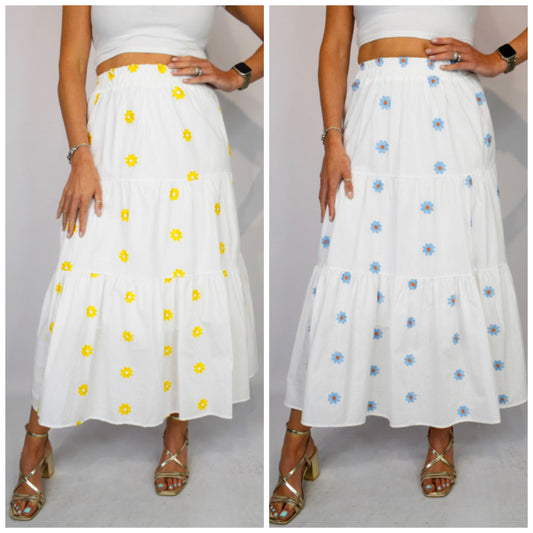 Two white skirts with floral patterns worn by a person on a plain background