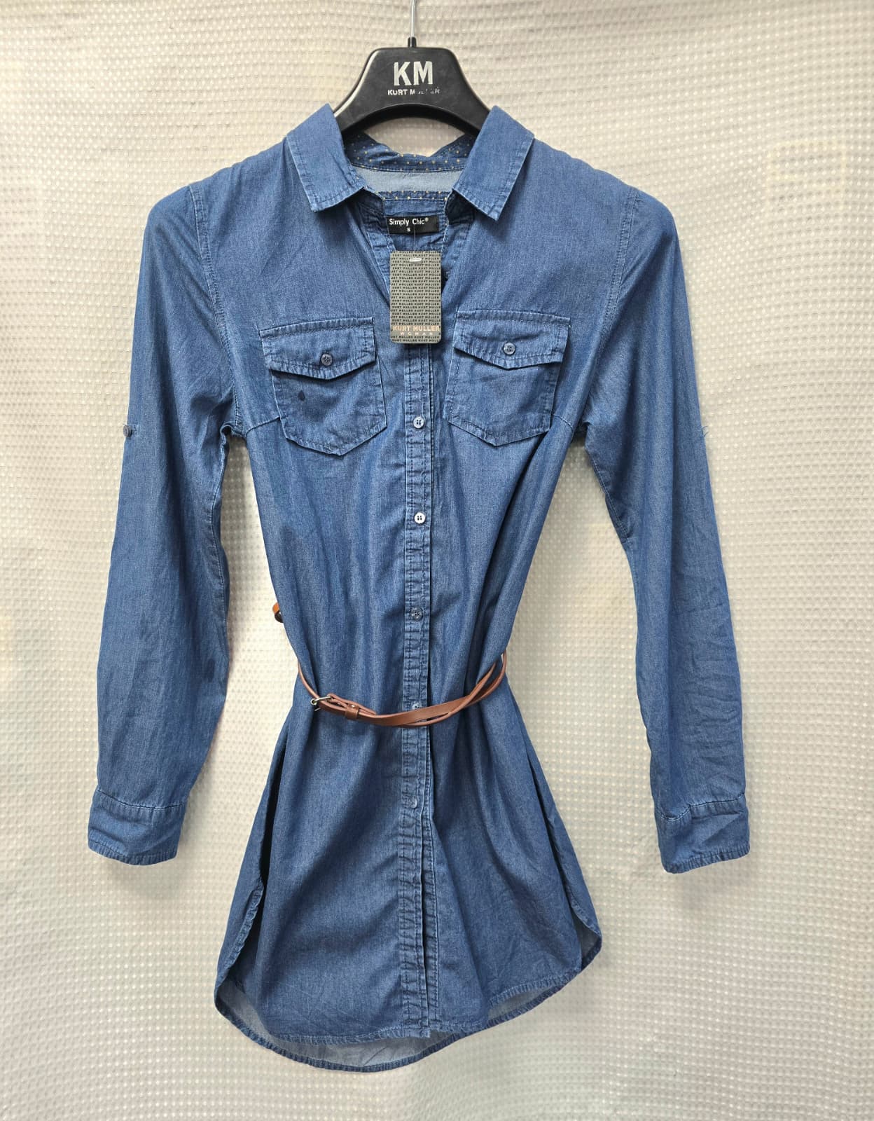 Blue denim shirt with a belt on a hanger against a neutral background