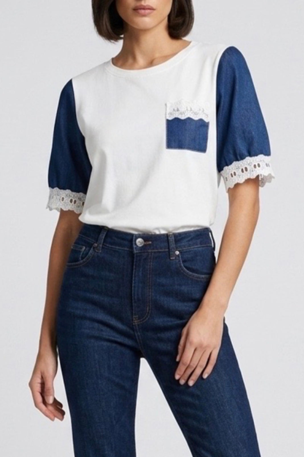 Woman wearing a white and blue top with lace details and dark blue jeans on a white background