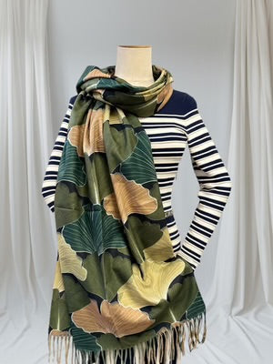 Mannequin wearing a striped sweater with a large green and beige patterned scarf draped over it against a white background.