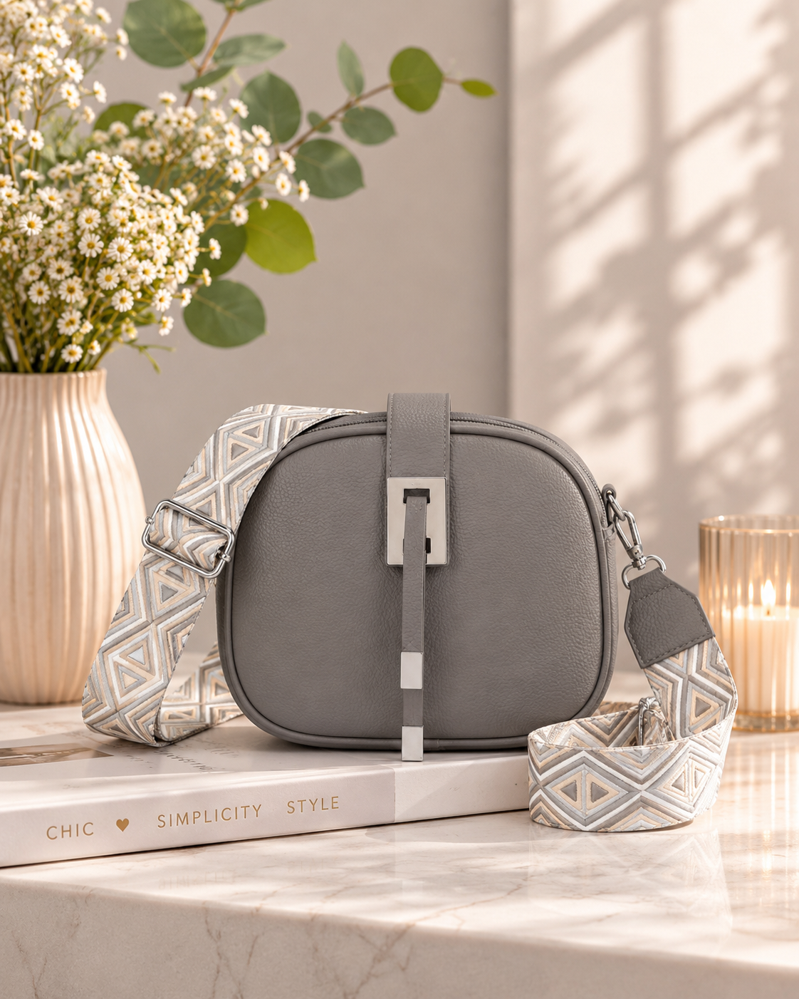 Gray bag with patterned strap on a surface with books and flowers in the background