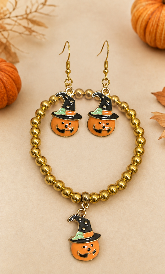 Gold beaded bracelet and matching drop earrings featuring orange pumpkin charms wearing black witch hats with green trim, displayed on a beige background with autumn leaves and pumpkins.