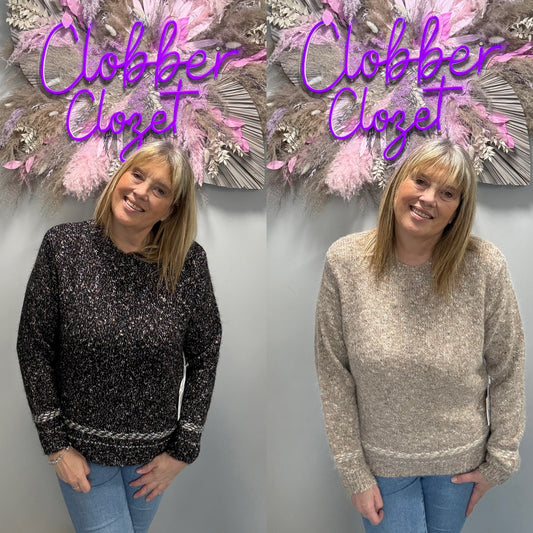 A side-by-side comparison of a woman wearing two different knit sweaters in front of a gray wall with a decorative floral arrangement. The left sweater is black with white speckles and a white patterned hem, and the right sweater is a heathered oatmeal beige.