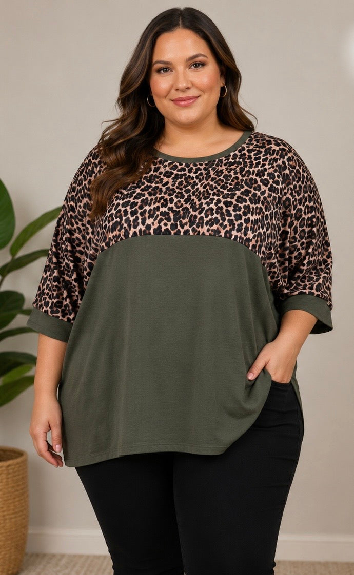 A woman modeling a colorblock top with a leopard print yoke and sleeves, an olive green body, and elbow-length sleeves, paired with black pants.