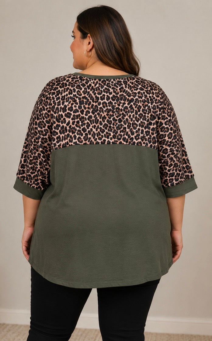 A woman shown from the back wearing a color-block top with a leopard print pattern on the upper back and shoulders and an olive green lower body, paired with black pants.