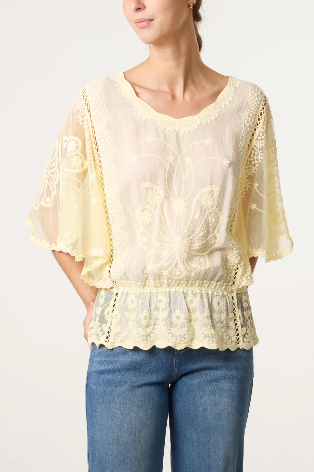 Woman wearing a Lemon Yellow Floral Lace Butterfly Sleeve Blouse and blue jeans on a white background