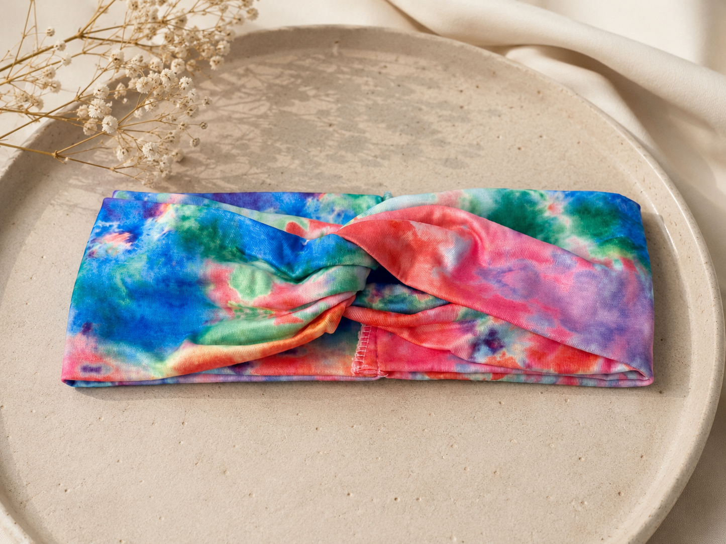 Colorful tie-dye headband on a textured surface with dried flowers.