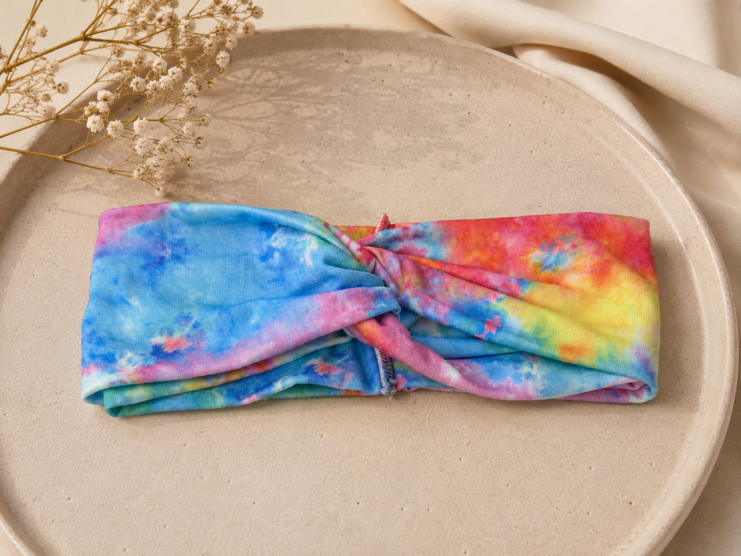 Colorful tie-dye headband on a beige plate with dried flowers.
