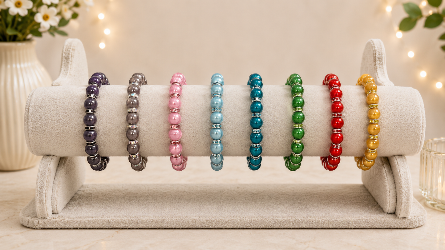 Seven beaded bracelets in different colors displayed on a white cylindrical stand. The bracelets include black, gray, pink, light blue, teal, green, red, and gold.