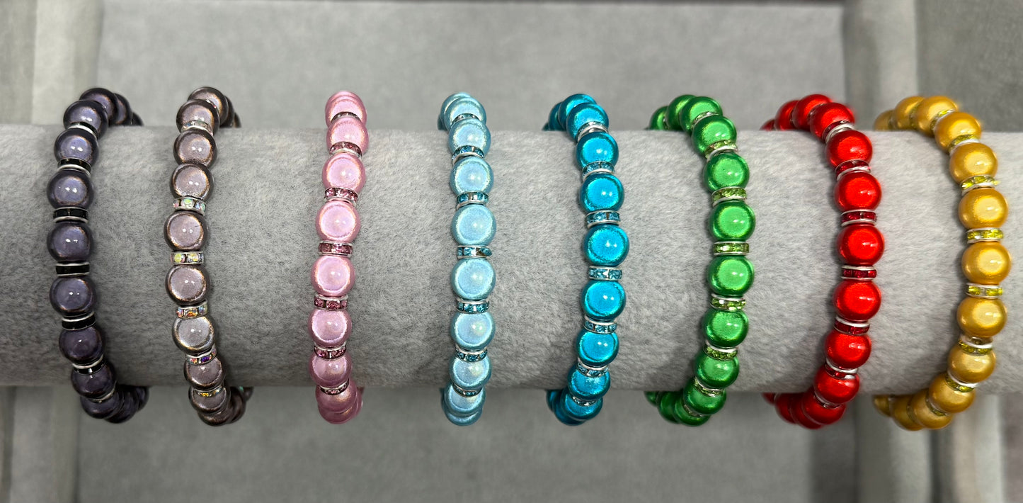 A set of colorful beaded bracelets displayed on a gray velvet jewelry stand. The bracelets feature round beads in shades of black, pink, light blue, green, red, and yellow, separated by small coloured sparkling spacer beads.