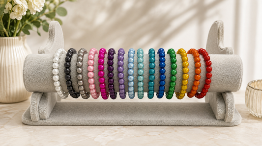 A set of colorful beaded stretch bracelets displayed on a gray velvet jewelry stand. The bracelets feature a rainbow of colors including white, black, gray, pink, purple, blue, green, yellow, orange, and red, arranged in a neat vertical sequence on the stand.