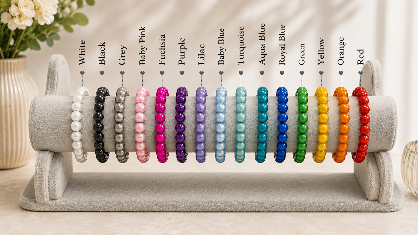 A display stand holding multiple beaded stretch bracelets in different colors, with color labels above each bracelet including White, Black, Grey, Baby Pink, Fuchsia, Purple, Lilac, Baby Blue, Turquoise, Royal Blue, Green, Yellow, Orange, and Red.